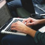 a man is typing on his laptop computer