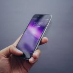 a hand holding a cell phone in front of a gray background