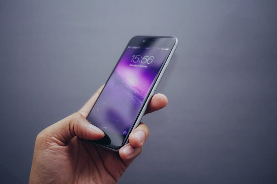 a hand holding a cell phone in front of a gray background