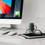 a computer monitor, keyboard, mouse and glasses on a desk