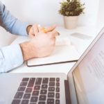 a man writing on a notebook next to a laptop