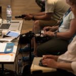 a group of people sitting around a table with laptops