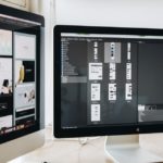 two computer monitors sitting on top of a wooden desk