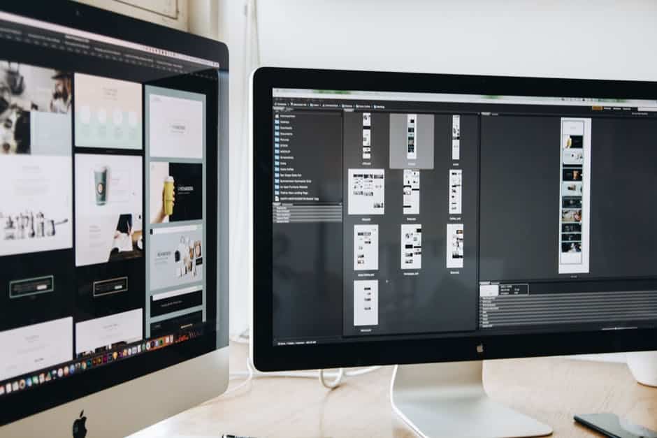 two computer monitors sitting on top of a wooden desk