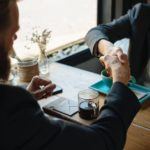 two people sitting at a table shaking hands