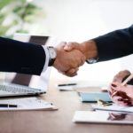 two people shaking hands in front of a laptop