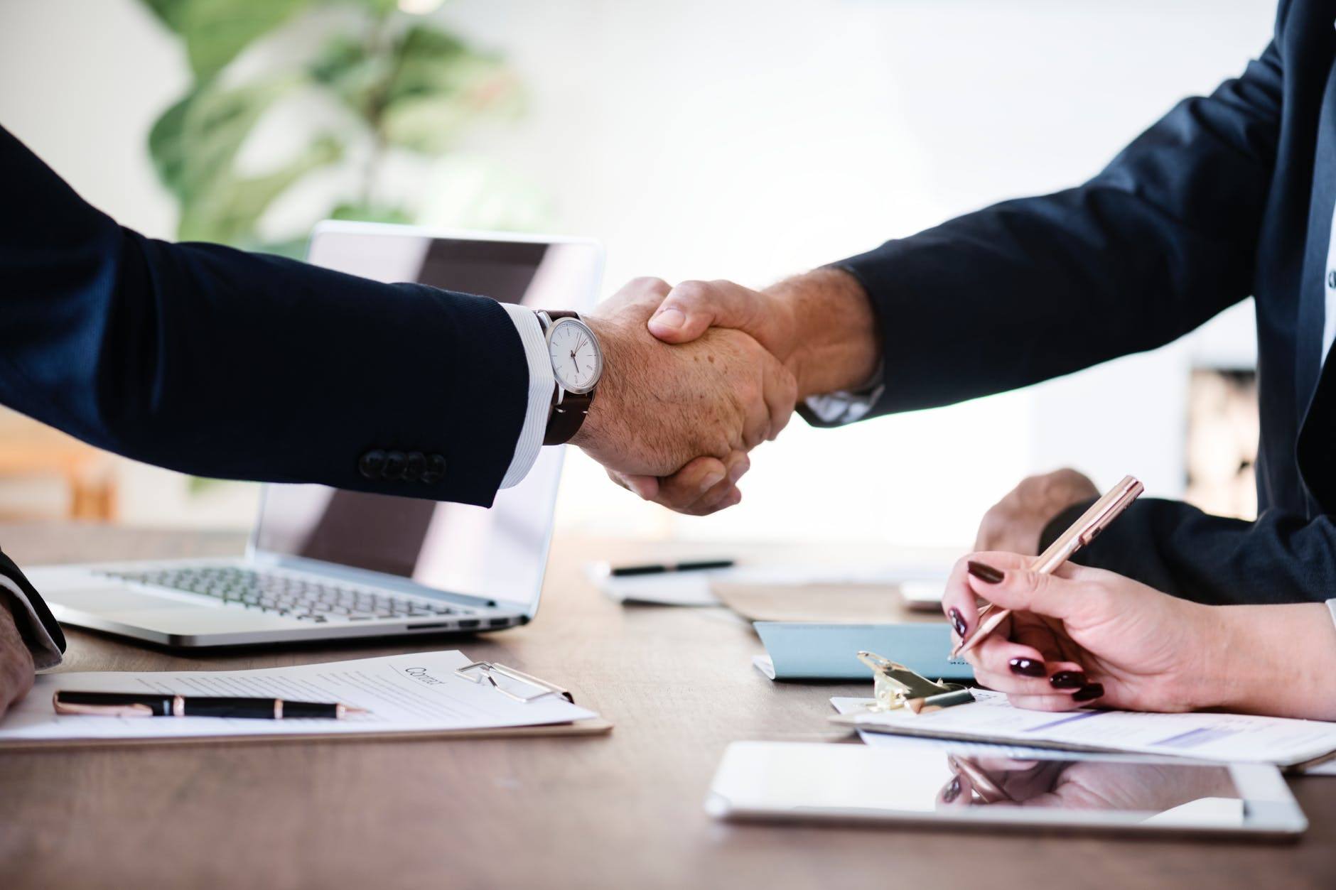 two people shaking hands in front of a laptop