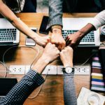 four people holding hands over a wooden table