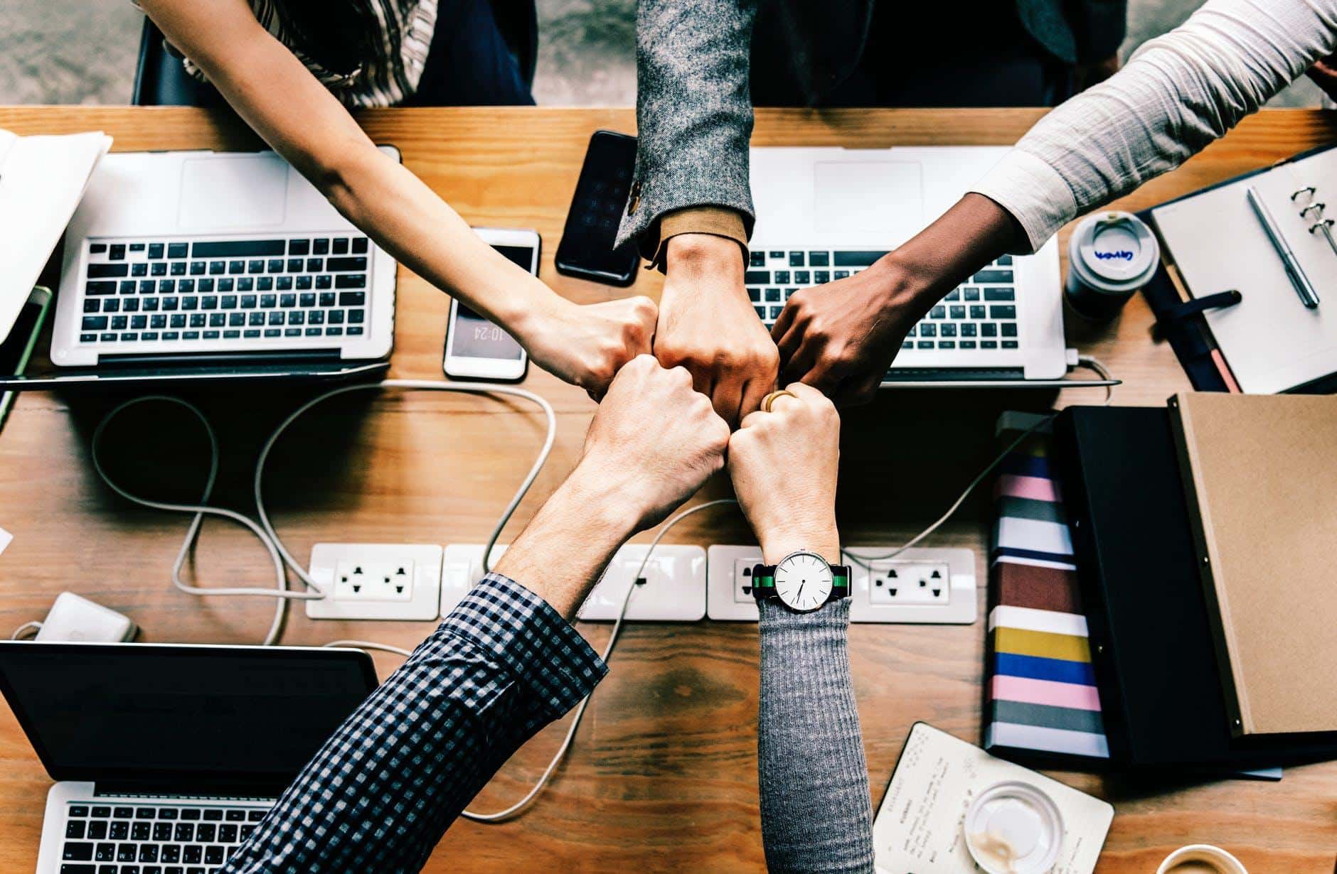 four people holding hands over a wooden table