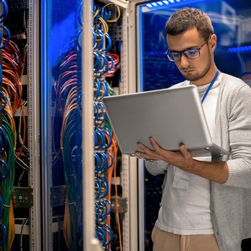 a man standing in front of a server holding a laptop