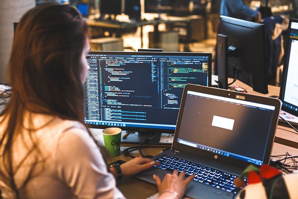 a woman sitting in front of two computer monitors